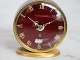 une horloge rouge à chiffres romains posée sur une table en marbre