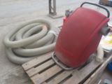 un réservoir rouge posé sur une palette, à côté d'un tuyau