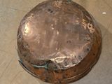 a large copper pan sitting on the floor with a handle