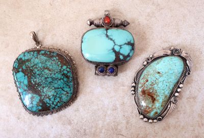 trois pendentifs ornés de turquoises et de pierres rouges, posés sur une table