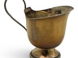 an antique brass milk pitcher on a stand on a white background