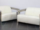 une paire de fauteuils en cuir blanc et chromé posés sur un sol en carrelage noir