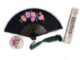 a black fan with pink flowers on it next to a ruler