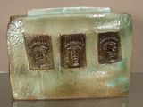 une sculpture en céramique représentant trois visages, posée sur une assiette verte