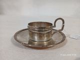 une tasse et une soucoupe en argent posées sur une soucoupe, sur une table