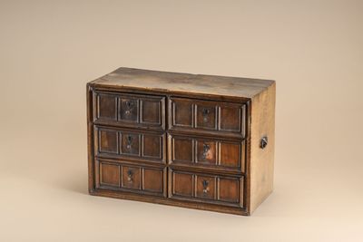 a small wooden chest of drawers on a beige background