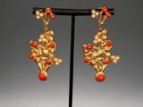 a pair of gold and coral earrings on a black stand