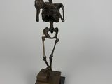 une statue en bronze représentant un squelette tenant un crâne humain, posée sur un socle en bois