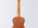 an old wooden guitar hanging from a string on a white wall