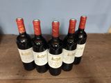 six bottles of red wine are lined up on a wooden table