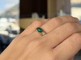 a woman ' s hand holding a ring with a green stone on it