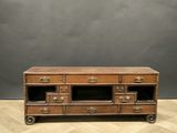 une vieille commode en bois à quatre tiroirs, montée sur roulettes, posée sur un parquet