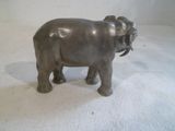 statue d'un éléphant debout sur une surface blanche, avec un mur blanc en arrière-plan