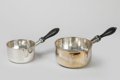 pair of silver saucepans with black handles on a white background