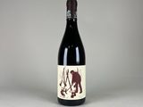 the bottle of red wine is sitting on a white surface