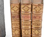 three old books are stacked on top of each other on a white surface