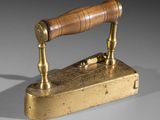 an old fashioned brass iron with a wooden handle on a gray surface
