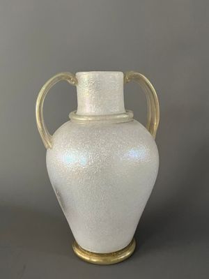 un vase blanc muni d'une anse dorée, posé sur une table