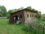 a small wooden building in the middle of a grassy field