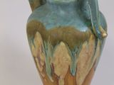 a blue and green vase with a handle on a white surface