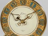 a gold clock on a stand with a blue and white clock face