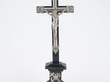 une croix en argent posée sur un socle noir, sur fond blanc