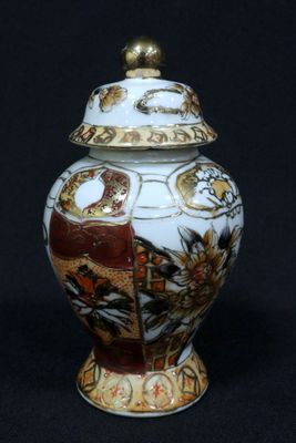 a white and gold vase with a lid on a black background