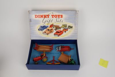 une boîte contenant des jouets Dinky Toys, comprenant un camion rouge, une voiture rouge, un camion rouge et une boîte bleue sur laquelle est collé un autocollant jaune