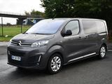 Une camionnette Citroën garée sur un parking, avec un pont en arrière-plan