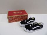 une paire de Vans noires et blanches sans lacets, à côté d'une boîte de Vans rouges et blanches