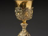 an ornate gold goblet on a stand with a black background