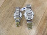 pair of silver watches on a wooden surface with a tag