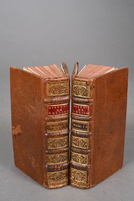 two old books are stacked on top of each other on a gray surface