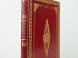 un vieux livre rouge avec des bordures dorées posé sur une surface blanche