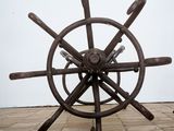 steering wheel of a ship on a brick floor in front of a white wall