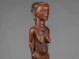 a wooden statue of a woman with a blue flower on her chest