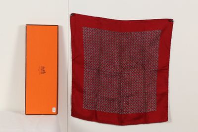 une boîte orange se trouve à côté d'une écharpe rouge sur une surface blanche