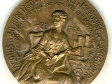 La médaille est en or et représente une femme assise sur une chaise.