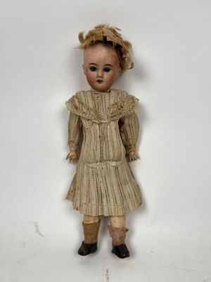 une poupée à l'ancienne, vêtue d'une robe et de chaussures, posée sur une surface blanche