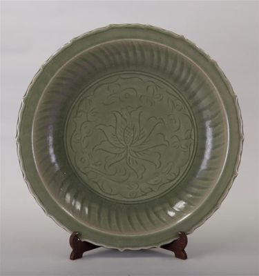 une assiette verte ornée d'un motif, posée sur un support en bois