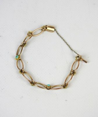 un gros plan d'un bracelet en or orné de perles de turquoise sur un fond blanc