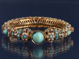 un gros plan d'un bracelet en or et turquoise posé sur une surface noire
