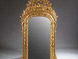 an ornately carved mirror with a gold frame on a white surface
