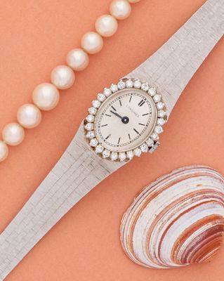 une image représentant une montre pour femme ornée de perles et d'un coquillage sur fond rose