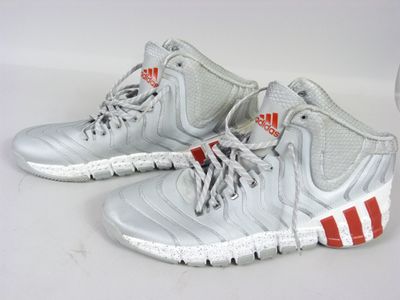 une paire de baskets Adidas argentées et rouges posées sur une surface blanche