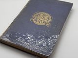 an old book sitting on a white table with a gold emblem on it
