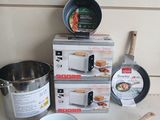 plusieurs casseroles et poêles posées sur un plan de travail, à côté d'une boîte de provisions
