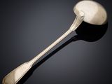 une cuillère en argent et un repose-cuillère posés sur une surface noire, sur fond noir