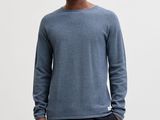 a man in a blue sweater and black pants stands in front of a white wall