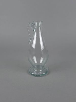 un vase en verre transparent muni d'une anse, posé sur un support gris